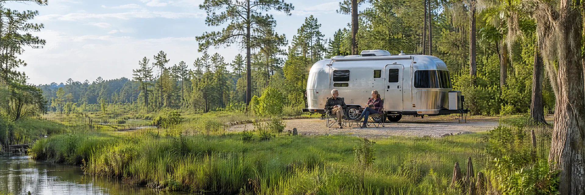 Illustration of campers enjoying relaxing at camp beside a rounded silver travel trailer in a fictional camping setting inspired by Vidor, TX.