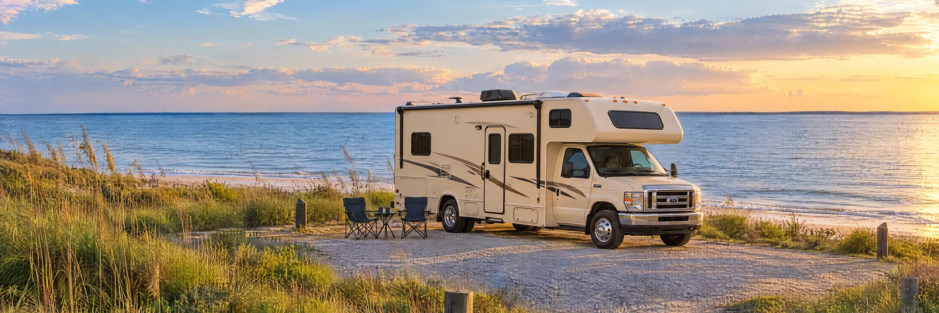 Illustration of a cream Class C motorhome with a modest overcab bunk at a fictional camping setting inspired by Cape Charles, VA.