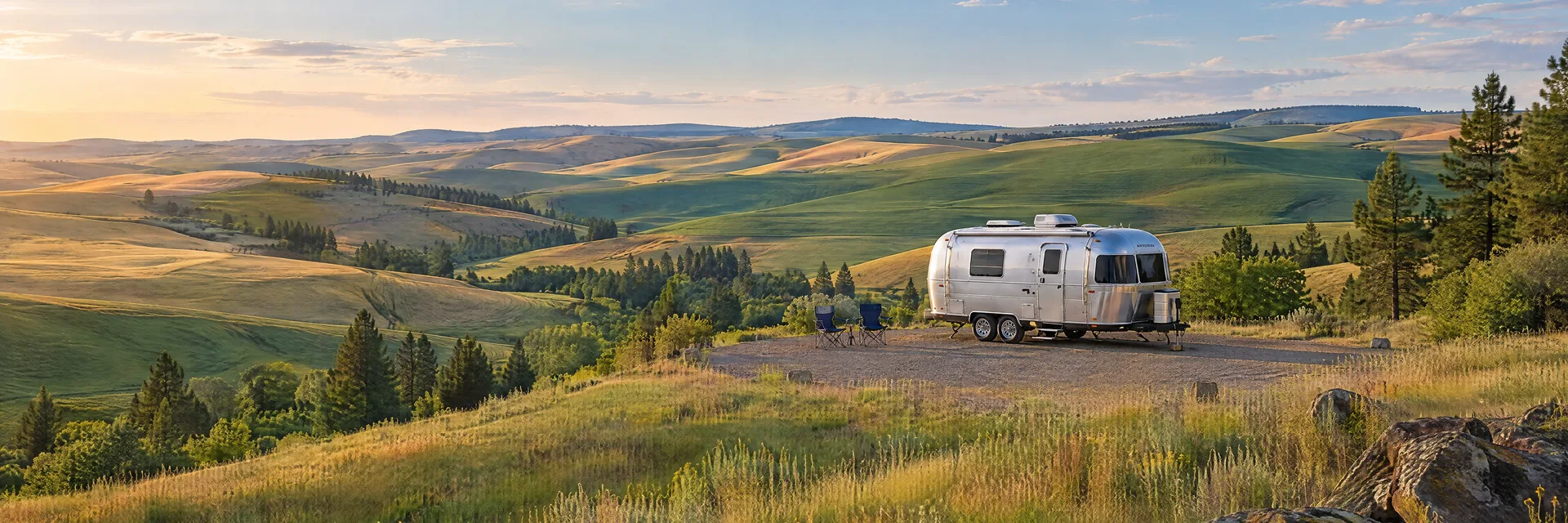 Illustration of a rounded silver travel trailer at a fictional camping setting inspired by Pullman, WA.