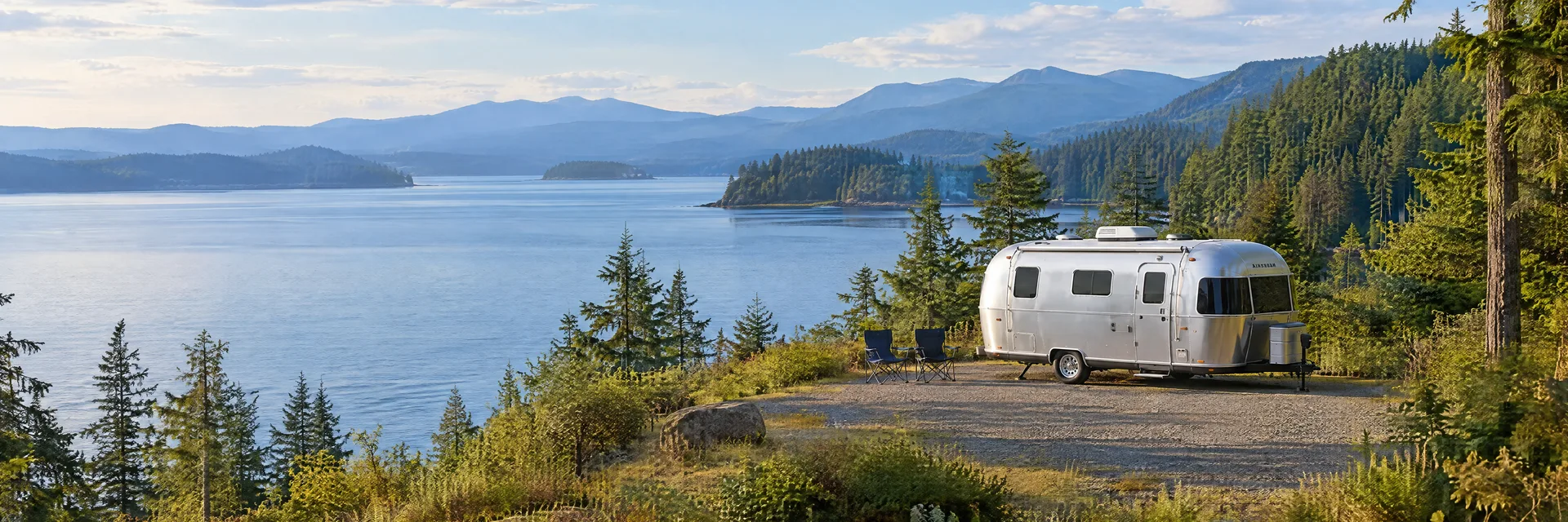 Illustration of a rounded silver travel trailer at a fictional camping setting inspired by Shelton, WA.