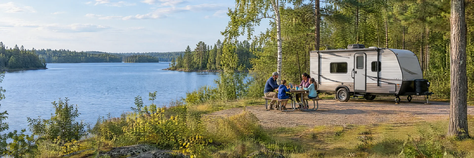 Illustration of campers enjoying a family picnic beside a compact travel trailer in a fictional camping setting inspired by Birchwood, WI.