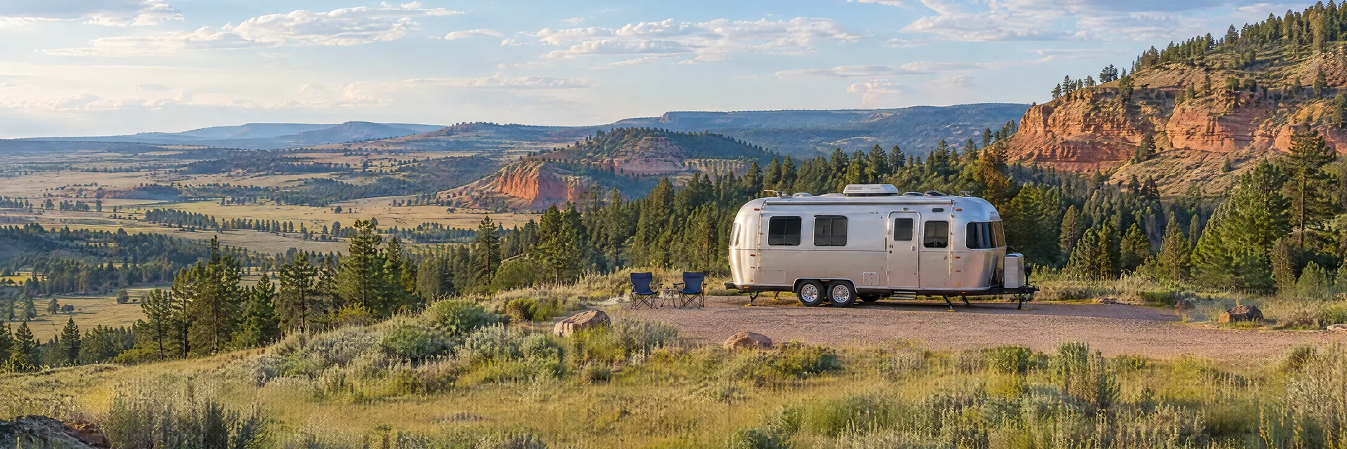 Illustration of a rounded silver travel trailer at a fictional camping setting inspired by Devils Tower, WY.