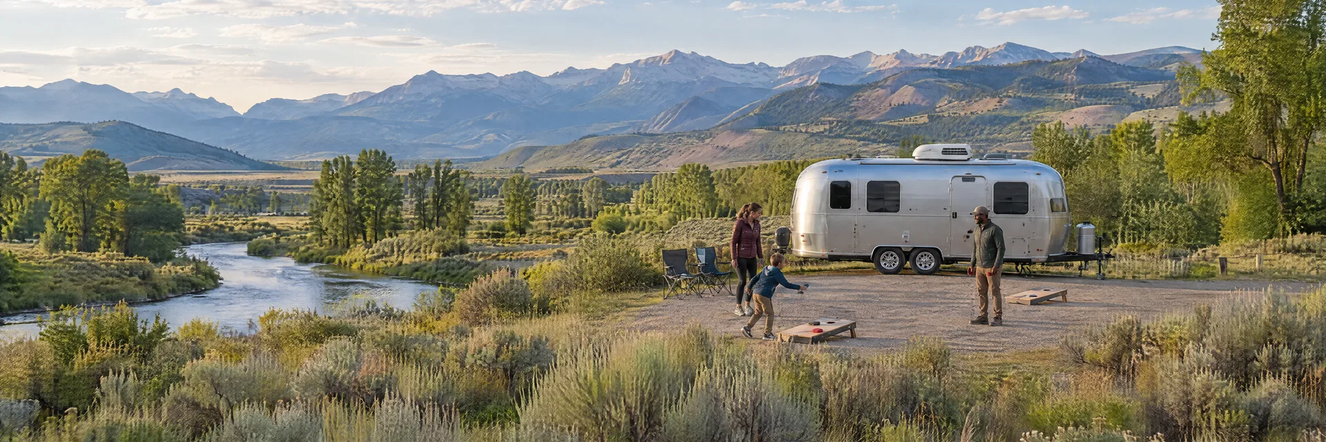 Illustration of campers enjoying family campsite activities beside a rounded silver travel trailer in a fictional camping setting inspired by Saratoga, WY.