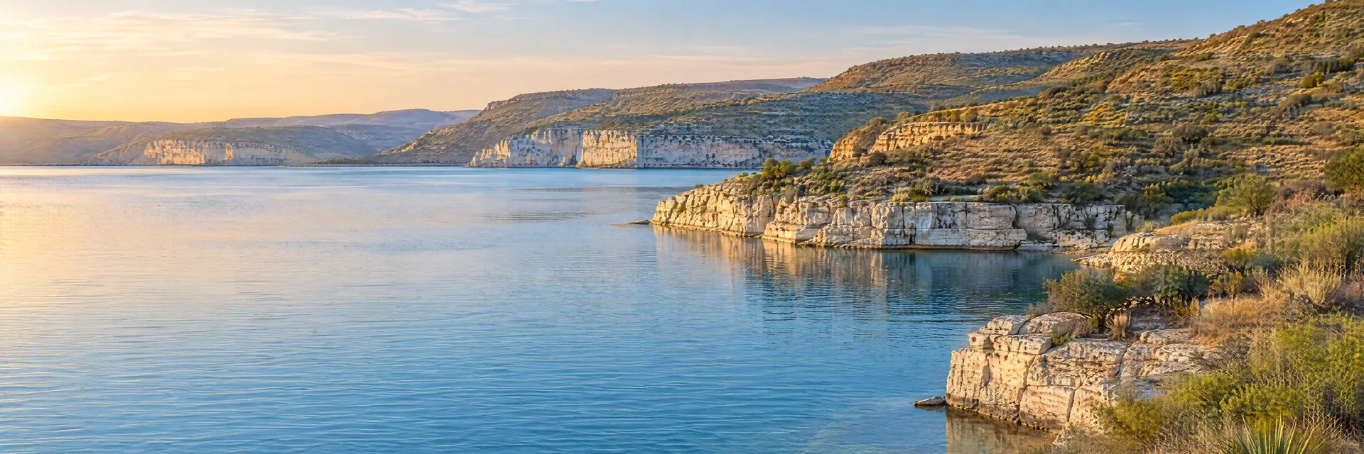 AI-generated illustration inspired by Amistad Reservoir: clear blue water, pale limestone cliffs and arid scrub-covered rolling hills in southwest Texas.