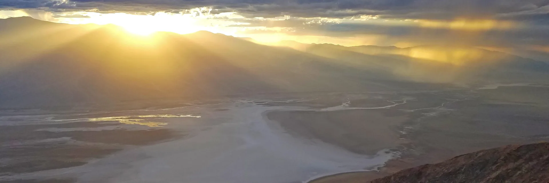 Sunlight breaking through clouds above the salt-filled valley in Death Valley National Park.