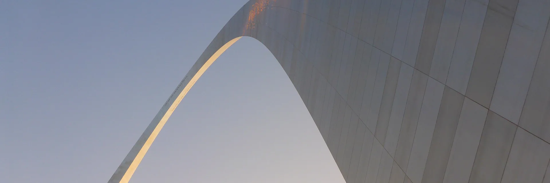 The curved stainless-steel surface of the Gateway Arch against the sky.
