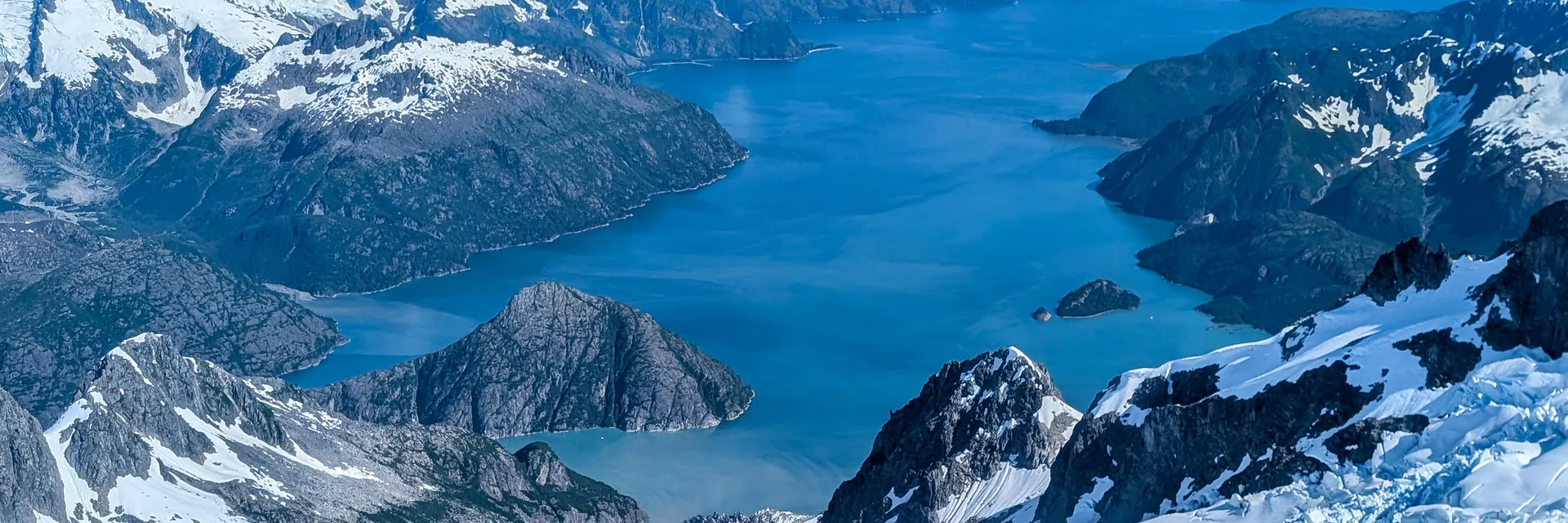 Aerial view of a blue fjord between snowy mountains in Kenai Fjords National Park.