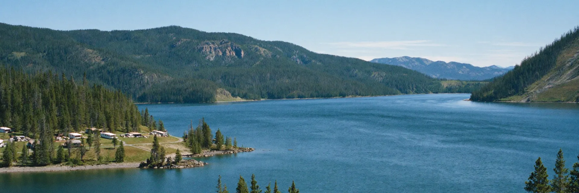 AI-generated illustration inspired by Lake Coeur d'Alene, ID: deep blue mountain lake with evergreen-forested hills, rocky points and a wooden dock, northern Idaho summer.