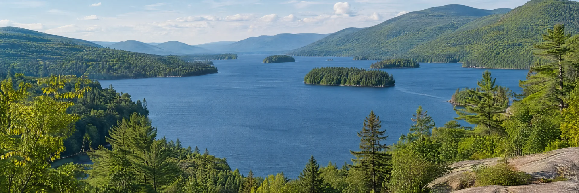 AI-generated illustration inspired by Lake George, New York, with wooded islands and rounded Adirondack mountains.