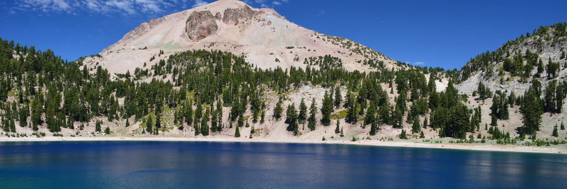Lassen Peak above a pine-lined blue lake in Lassen Volcanic National Park.