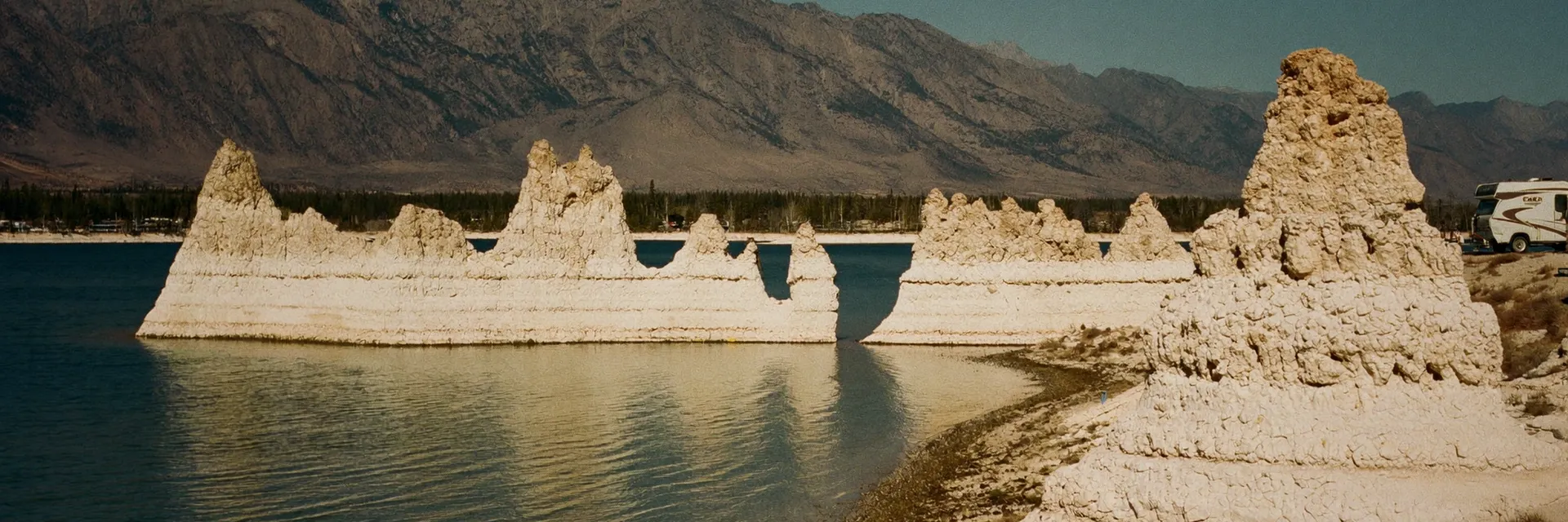 AI-generated illustration inspired by Mono Lake, CA: ancient saline lake with white tufa tower formations at the shore, the eastern Sierra Nevada mountains behind, calm reflective water.