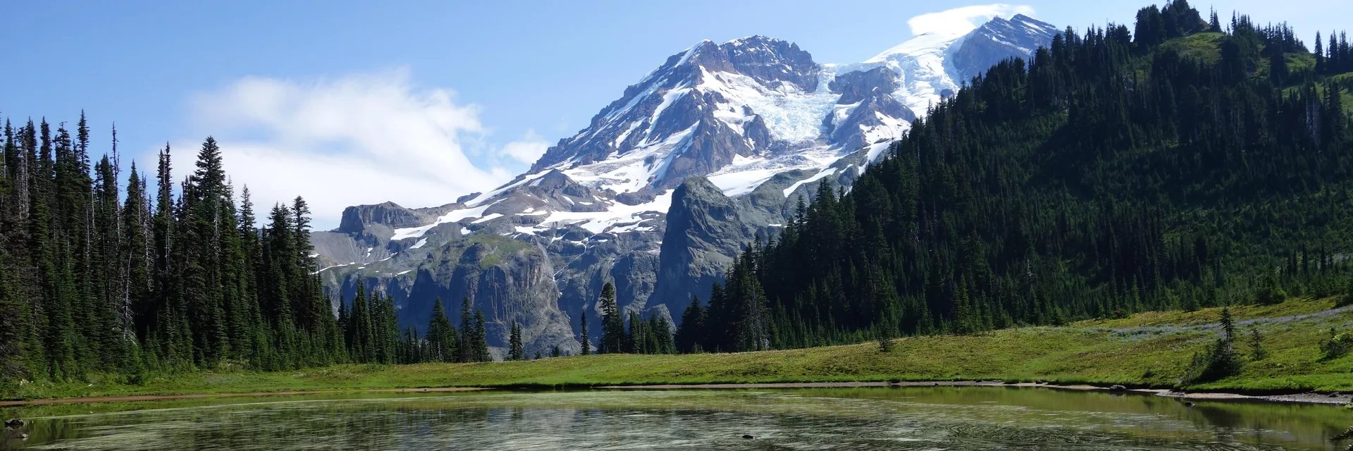 Snow-covered Mount Rainier above forested slopes and a still mountain lake.