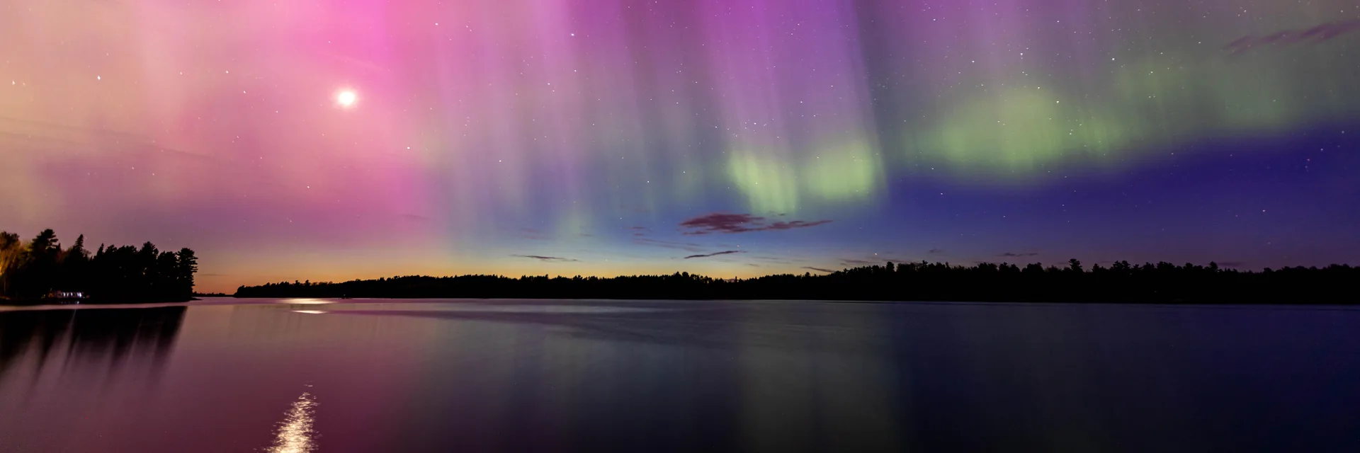 Pink and green northern lights reflected over a lake in Voyageurs National Park.
