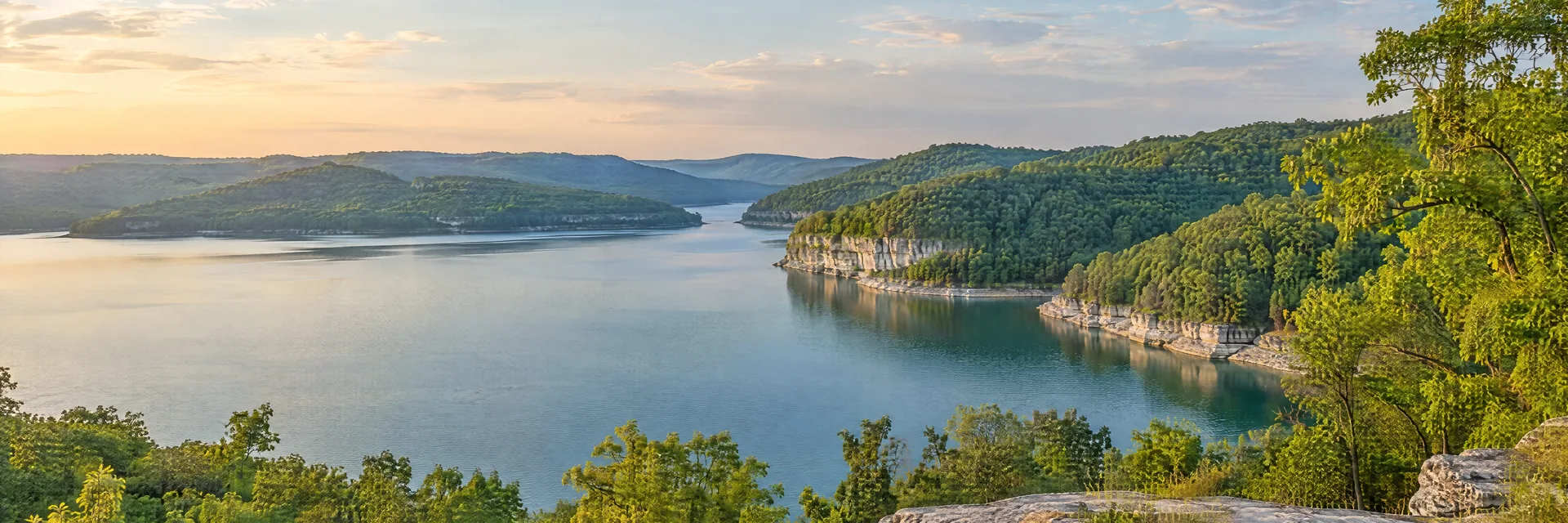 Illustration of representative natural scenery in Kentucky: hardwood-covered hills, quiet lake and pale limestone shoreline.