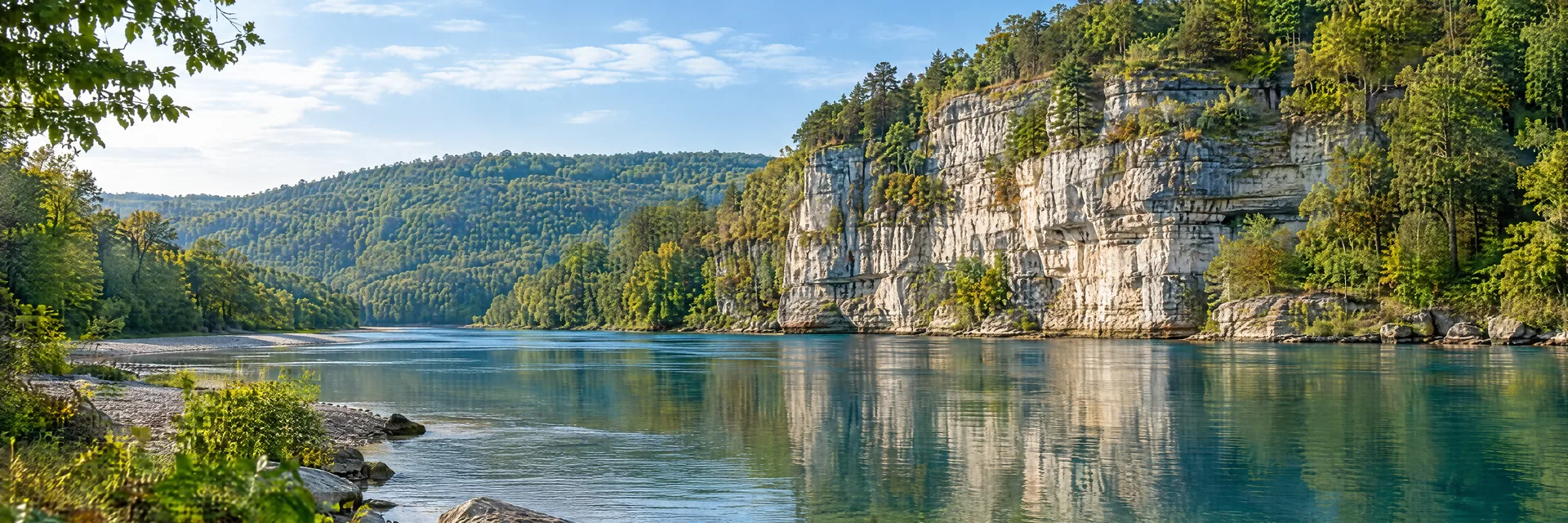 AI-generated illustration inspired by Arkansas: Ozark river landscape, pale limestone bluff reflected in clear blue-green water, wooded hills and a gravel shoreline.