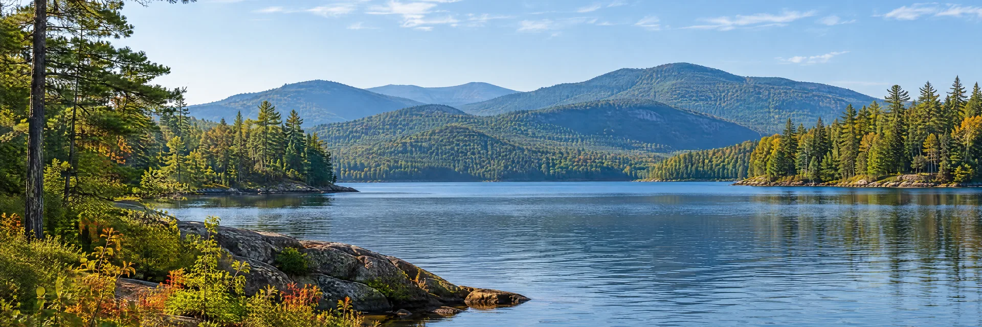AI-generated illustration inspired by New York: Adirondack-inspired lake landscape, low rocky shoreline, pine and mixed hardwood forest, layered rounded wooded mountains.