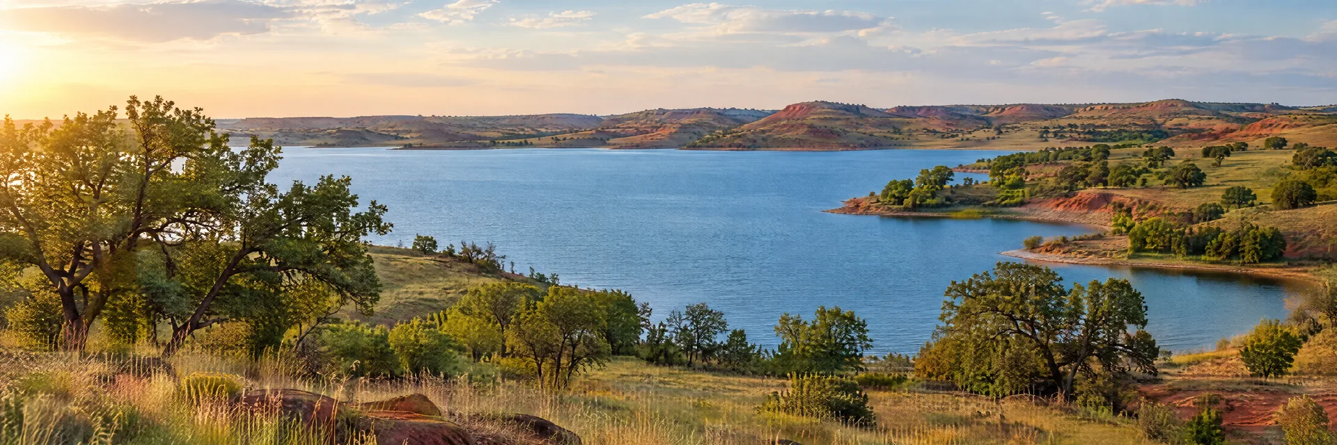 AI-generated illustration inspired by Oklahoma: Southern Great Plains lake and low rolling red-earth hills, prairie grasses, scattered oak trees and broad blue water.