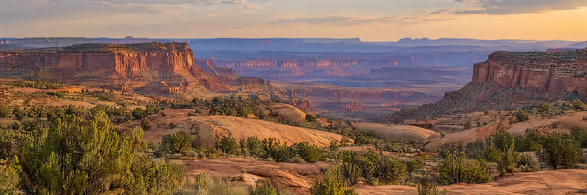 AI-generated illustration inspired by Utah: Open high-desert landscape with layered red sandstone mesas, rounded slickrock, scattered junipers and a broad distant canyon.