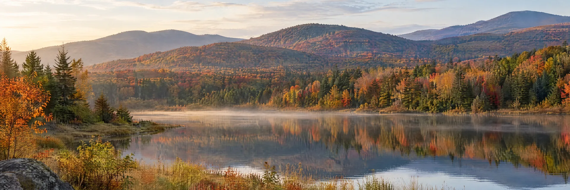 AI-generated illustration inspired by Vermont: Green Mountain landscape, rounded forested hills in restrained red and amber autumn colors, a calm pond and a natural grassy bank.