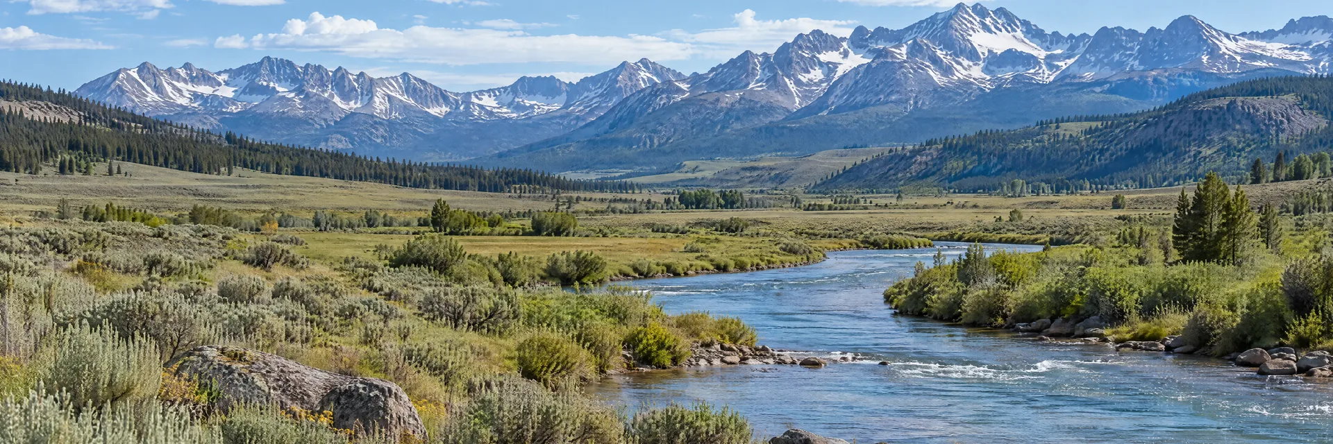 AI-generated illustration inspired by Wyoming: Wyoming mountain meadow, broad sagebrush valley and clear river, distant rugged snow-streaked Rocky Mountain ridges.